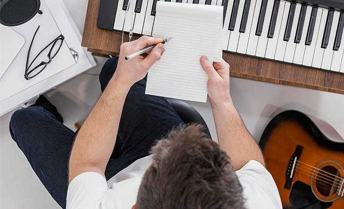 Mężczyzna piszący w notatniku obok gitary akustycznej w agencji marketingowej.
