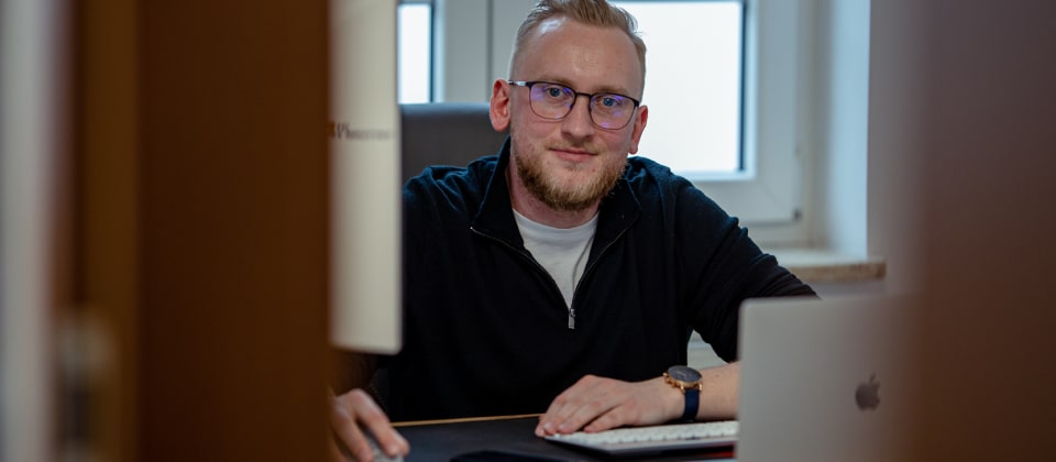 Mężczyzna w okularach siedzący przy biurku z laptopem i pracujący nad strategią marketingową i stronami internetowymi.