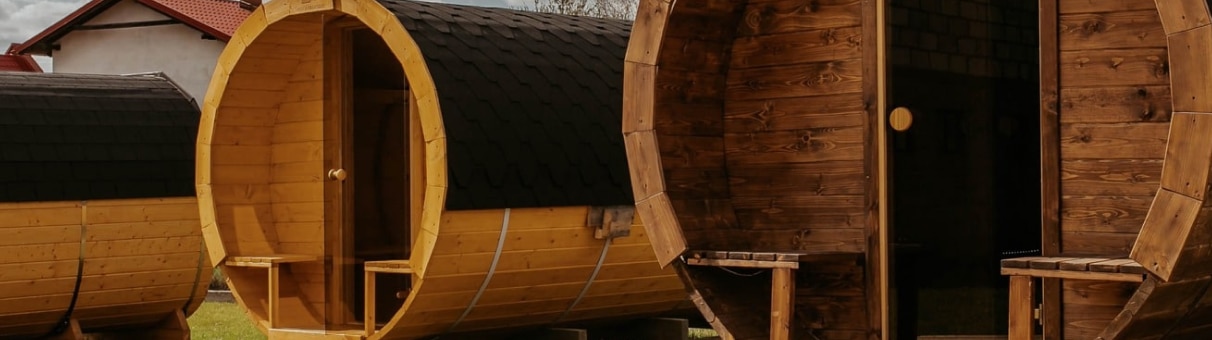 Drewniane kabiny w kształcie beczki na stojakach z otwartymi drzwiami.