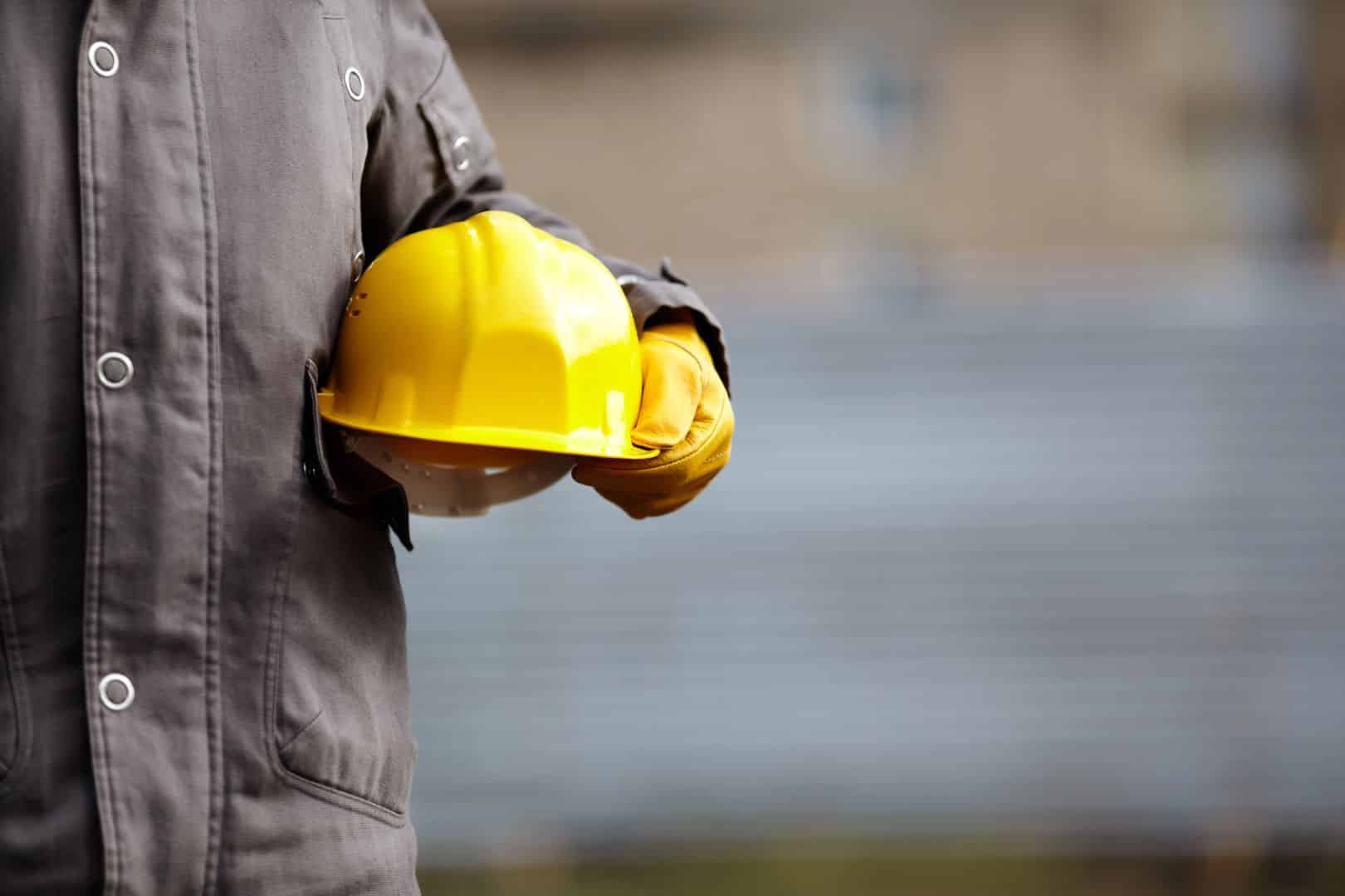 Pracownik budowlany trzymający żółty kask na placu budowy.