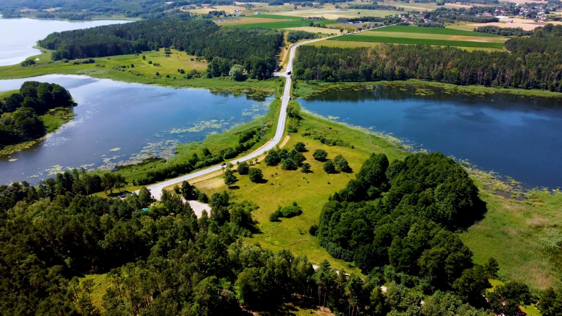 Widok z lotu ptaka na wąską drogę wijącą się przez bujny zielony krajobraz z jeziorami po obu stronach.