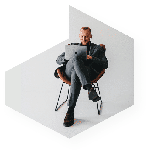 Osoba siedząca na nowoczesnym krześle, korzystająca z laptopa, ze skrzyżowanymi nogami i uśmiechnięta. Tło jest gładkie, białe.