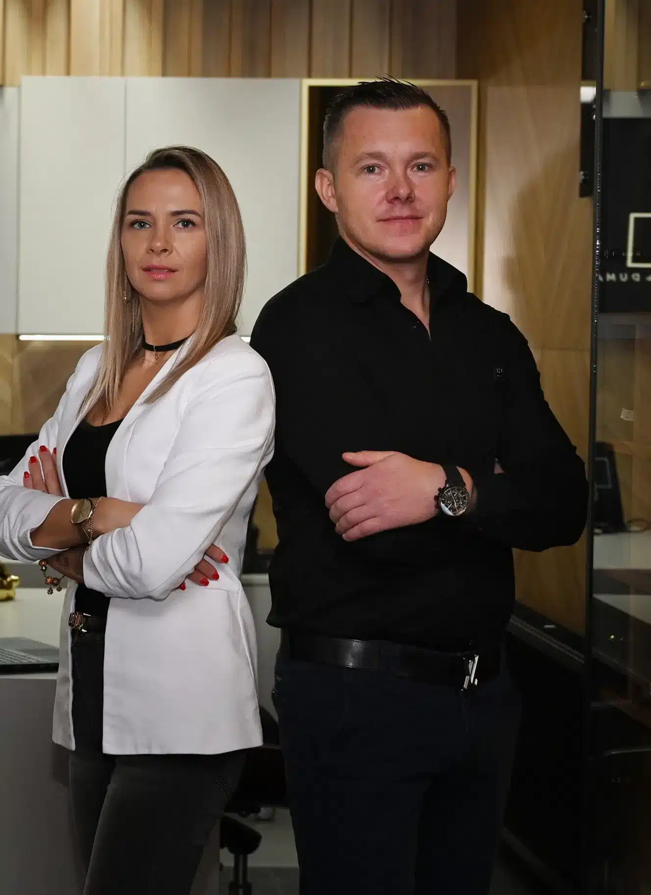 Kobieta w białej marynarce i mężczyzna w czarnej koszuli stoją tyłem do siebie ze skrzyżowanymi ramionami w nowoczesnym biurze.