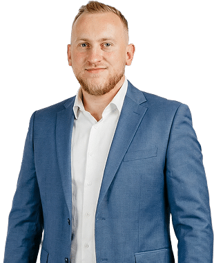 Mężczyzna z krótkimi blond włosami i brodą, ubrany w niebieską marynarkę i białą koszulę, stojący na białym tle.