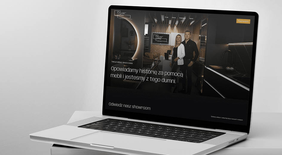 Laptop wyświetla stronę internetową przedstawiającą dwie osoby stojące w nowoczesnym salonie kuchennym z polskim tekstem i menu nawigacyjnym.